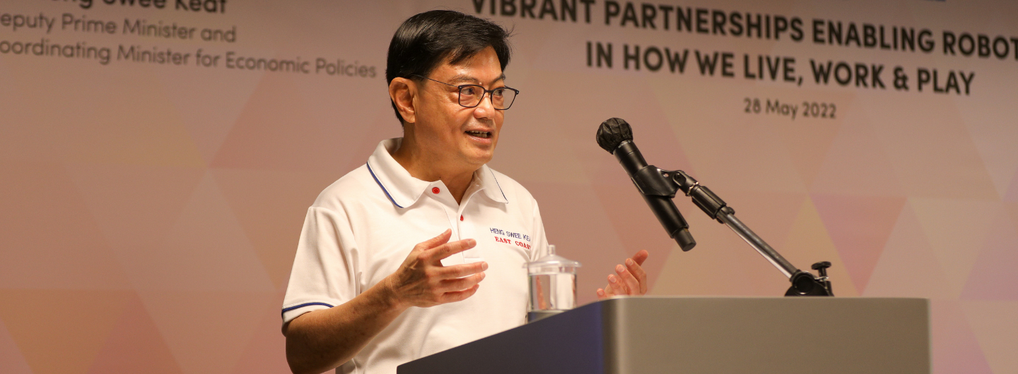 Heng Swee Keat at podium, speaking into microphone. He's wearing glasses and a white polo shirt.